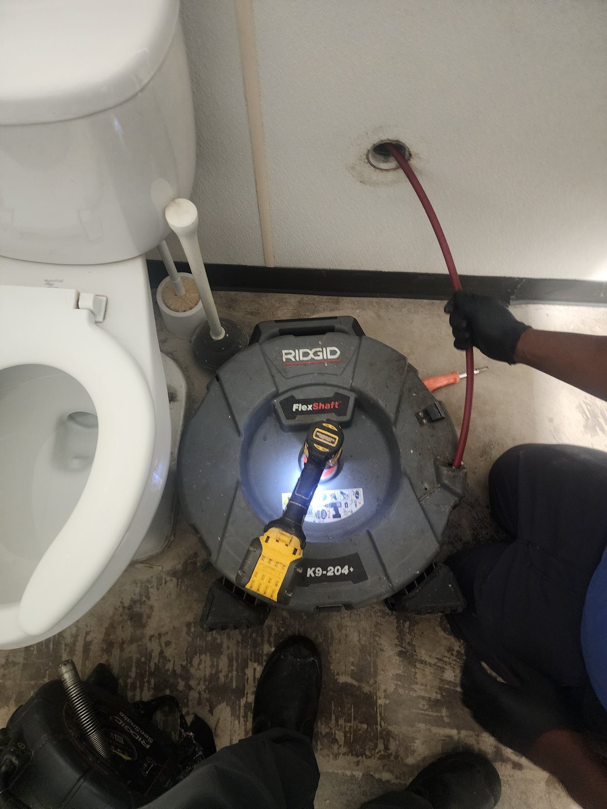 Drain cable run through a wall cleanout behind a toilet