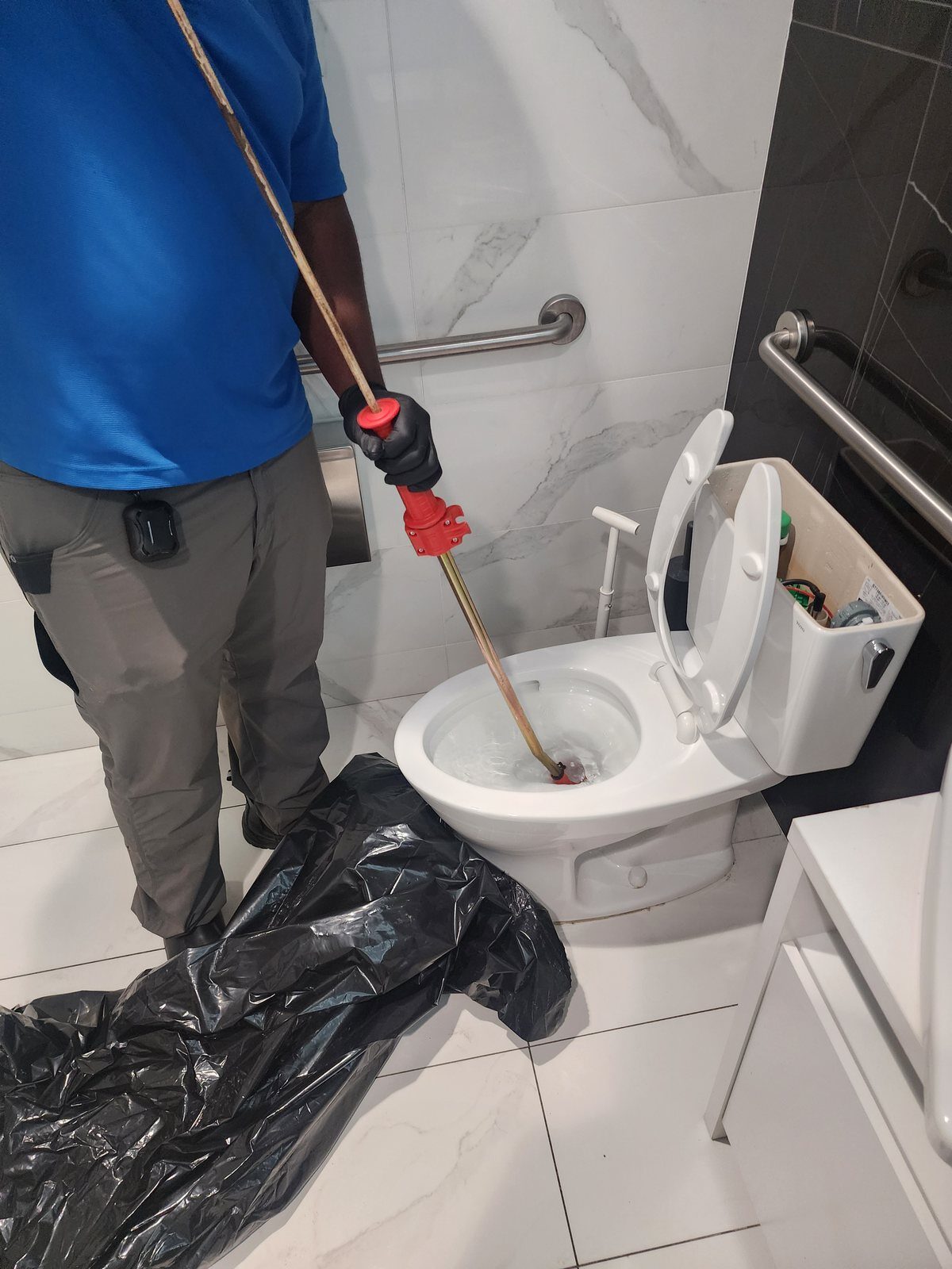 Day to Day Plumbing technician clearing a clogged toilet in a commercial restroom
