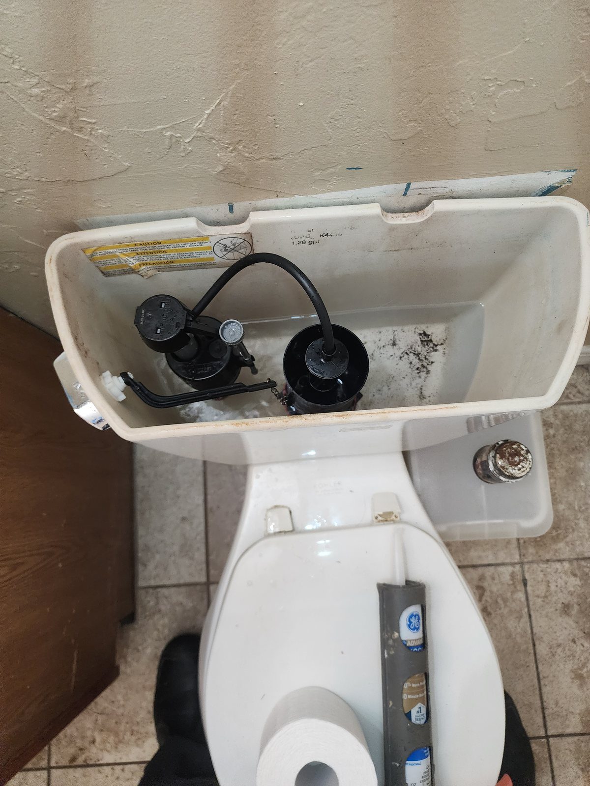 Worn fill valve and flapper inside a toilet tank before repair