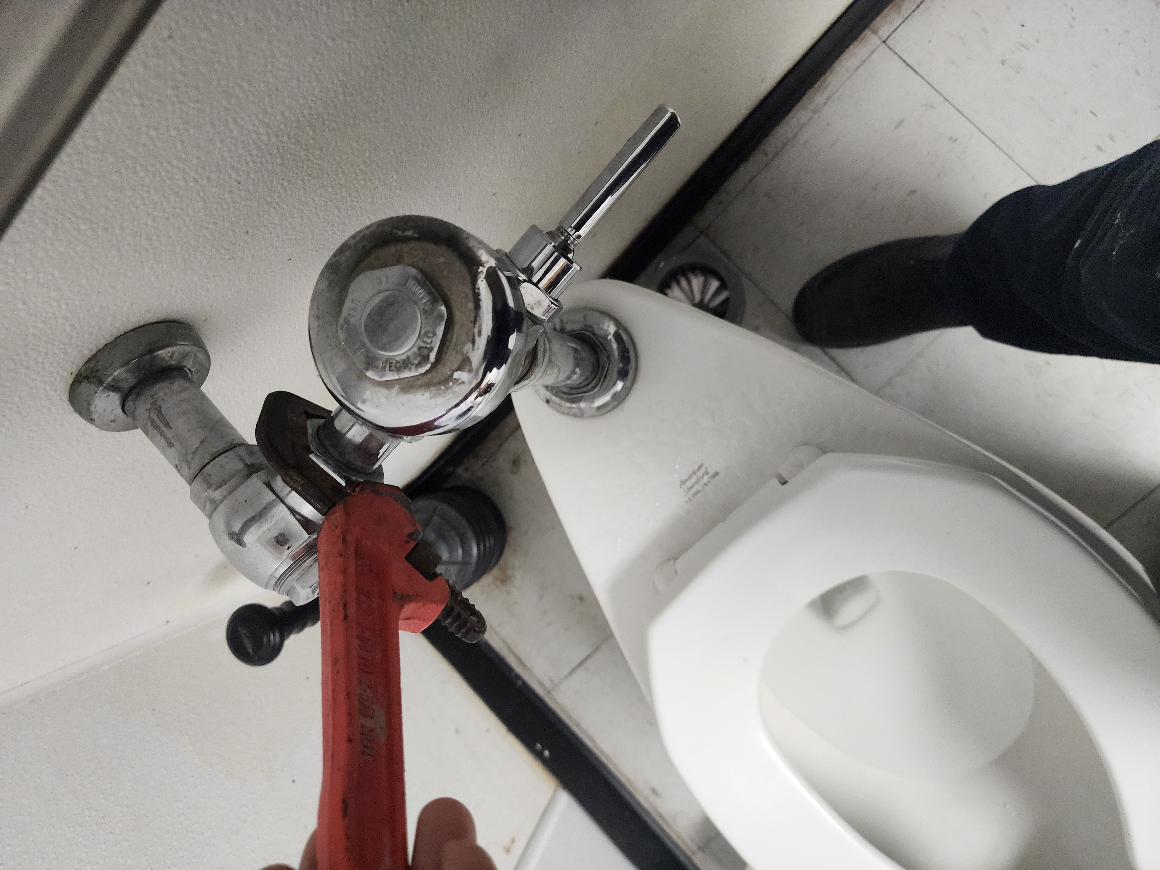Plumber repairing flushometer valve on commercial urinal Pittsburgh PA